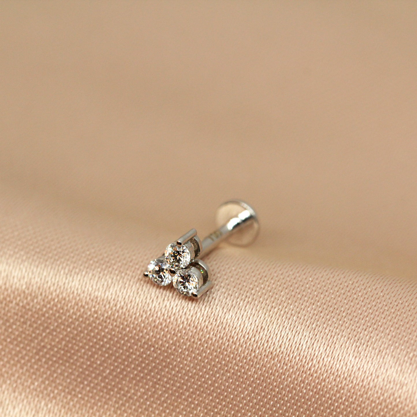 A single trinity stud earring with three interlocking gold elements set with clear natural diamonds, displayed on a beige background.